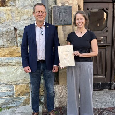 B&uuml;rgermeister J&uuml;rgen Akkermann und Standesbeamtin Stefanie Byl stehen nebeneinander vor dem Rathaus. Frau Byl pr&auml;sentiert ihre Ernennungsurkunde.